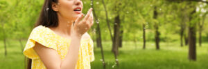 why isn't my allergy medication working woman sneezing outside in a yellow shirt with pollen floating in the air